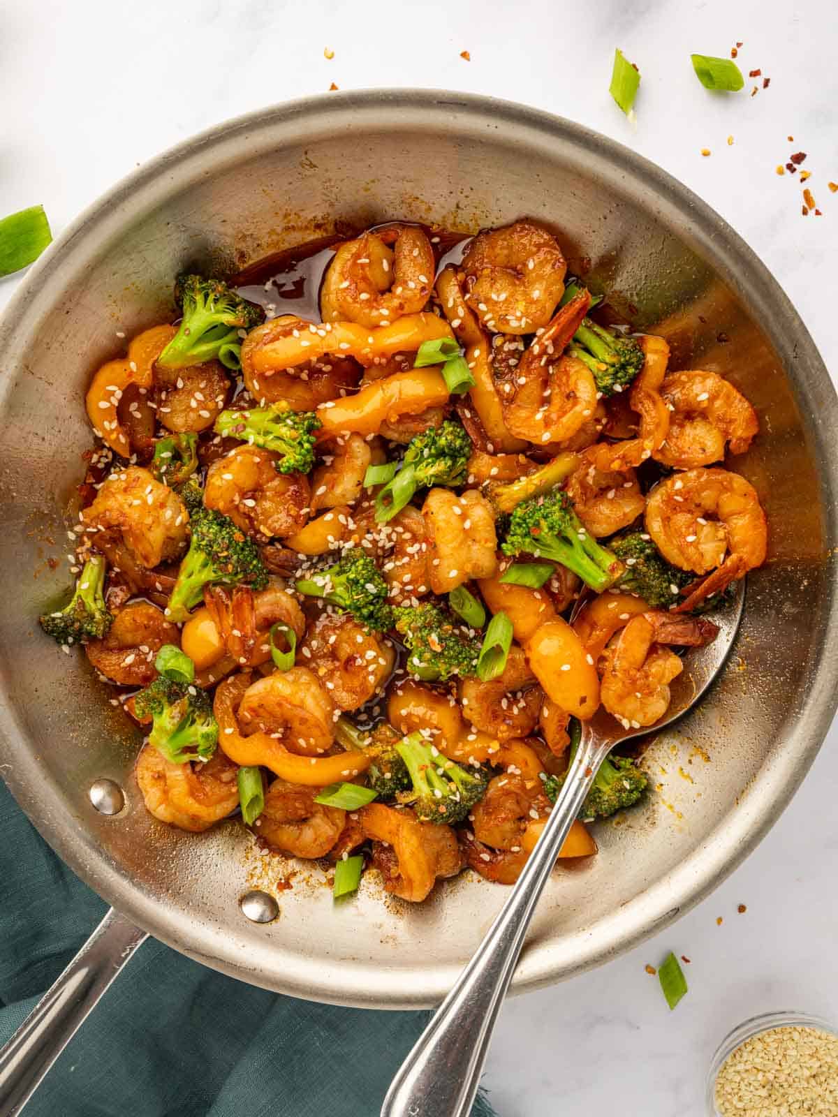 A spoon stirs shrimp in chili sauce.