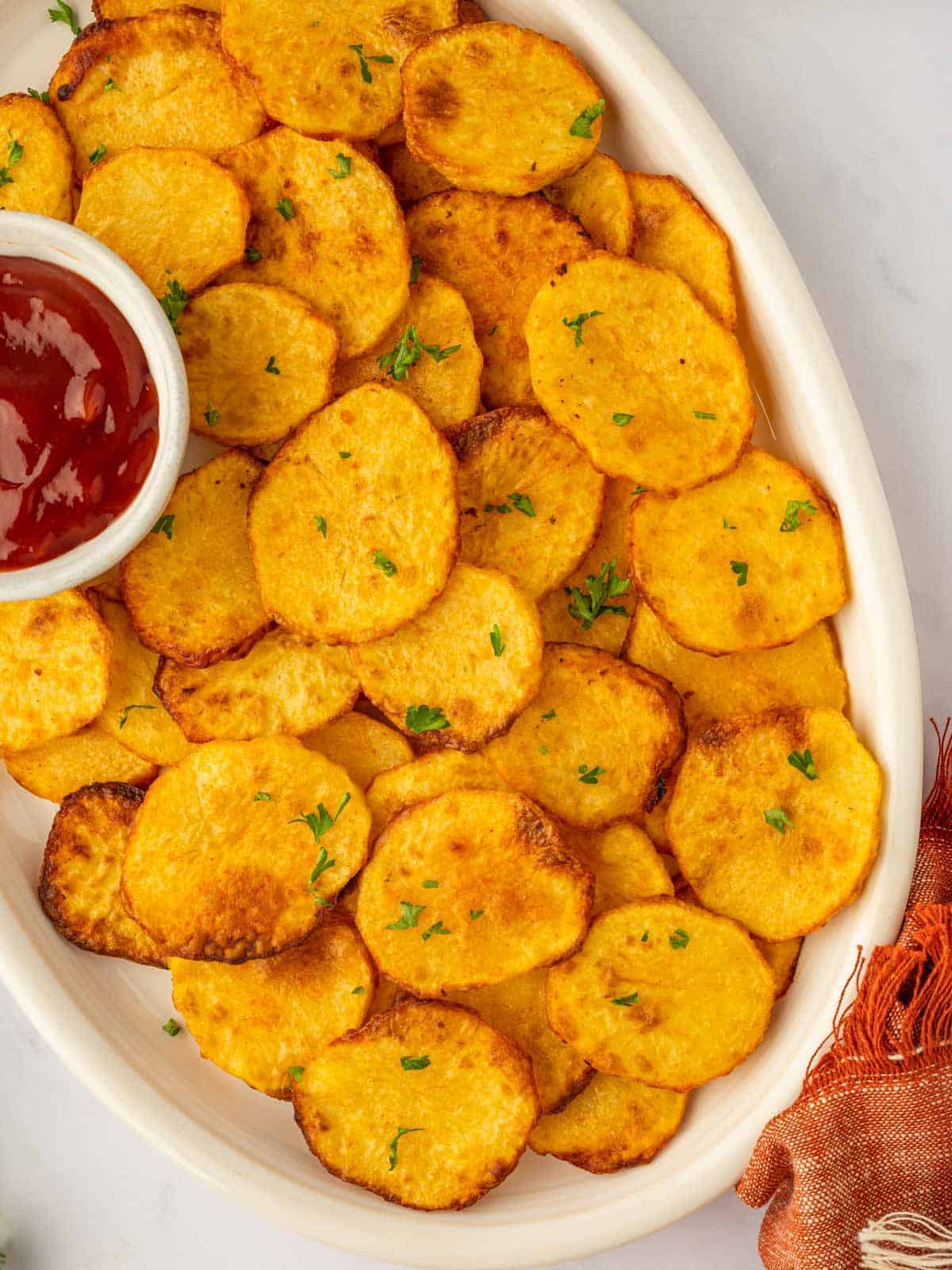 Potato chips are piled on a platter with ketchup.