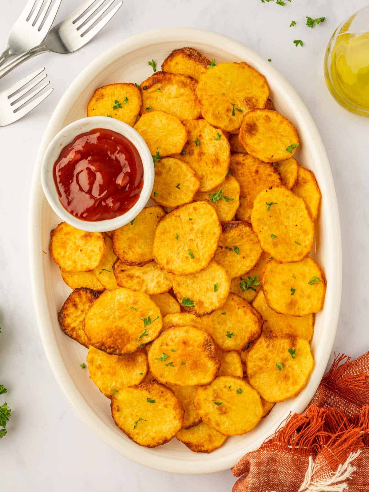 Ketchup sits on a large platter of crispy air fryer potato chips.