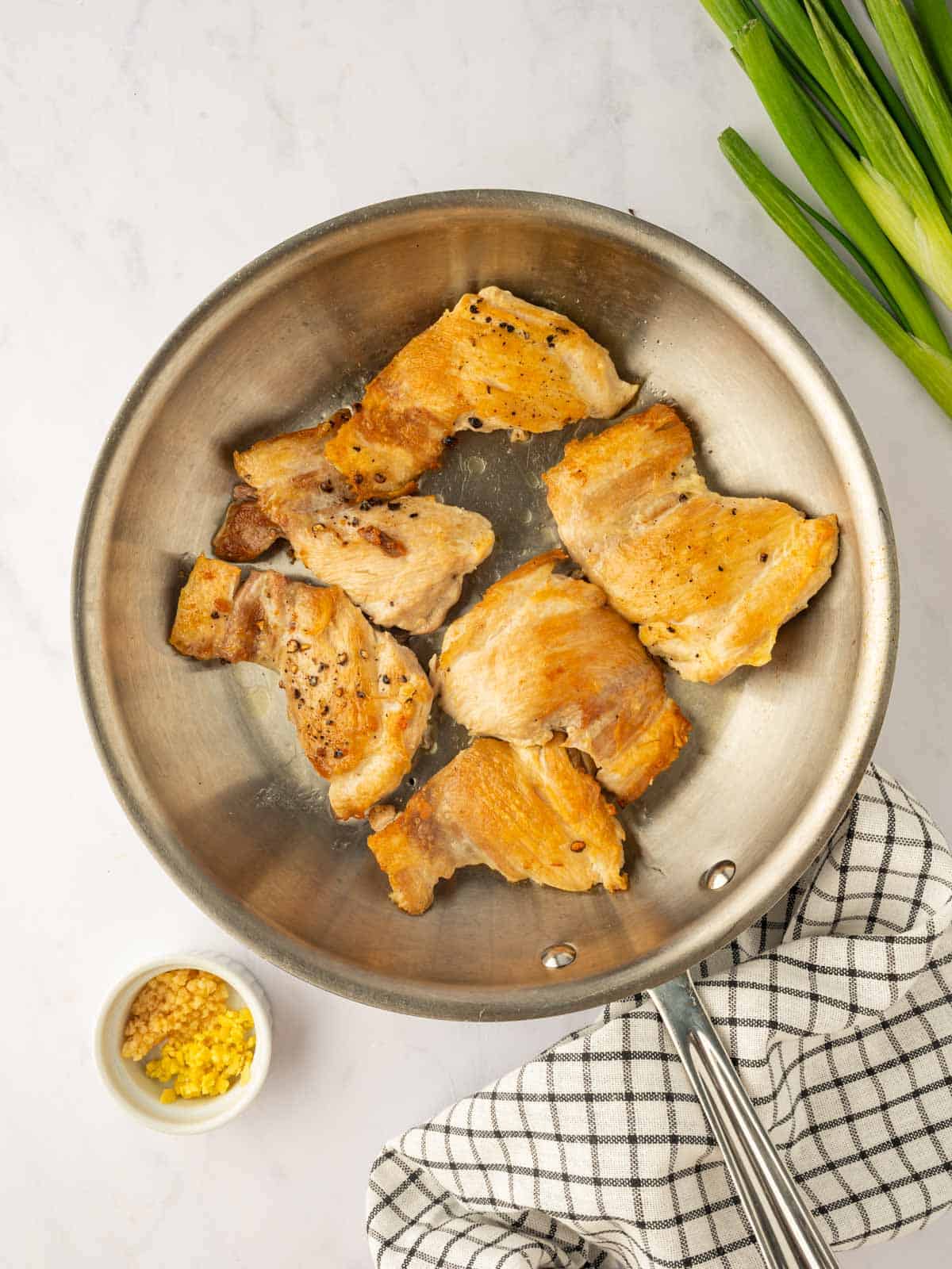 Chicken thighs are seared in a skillet.