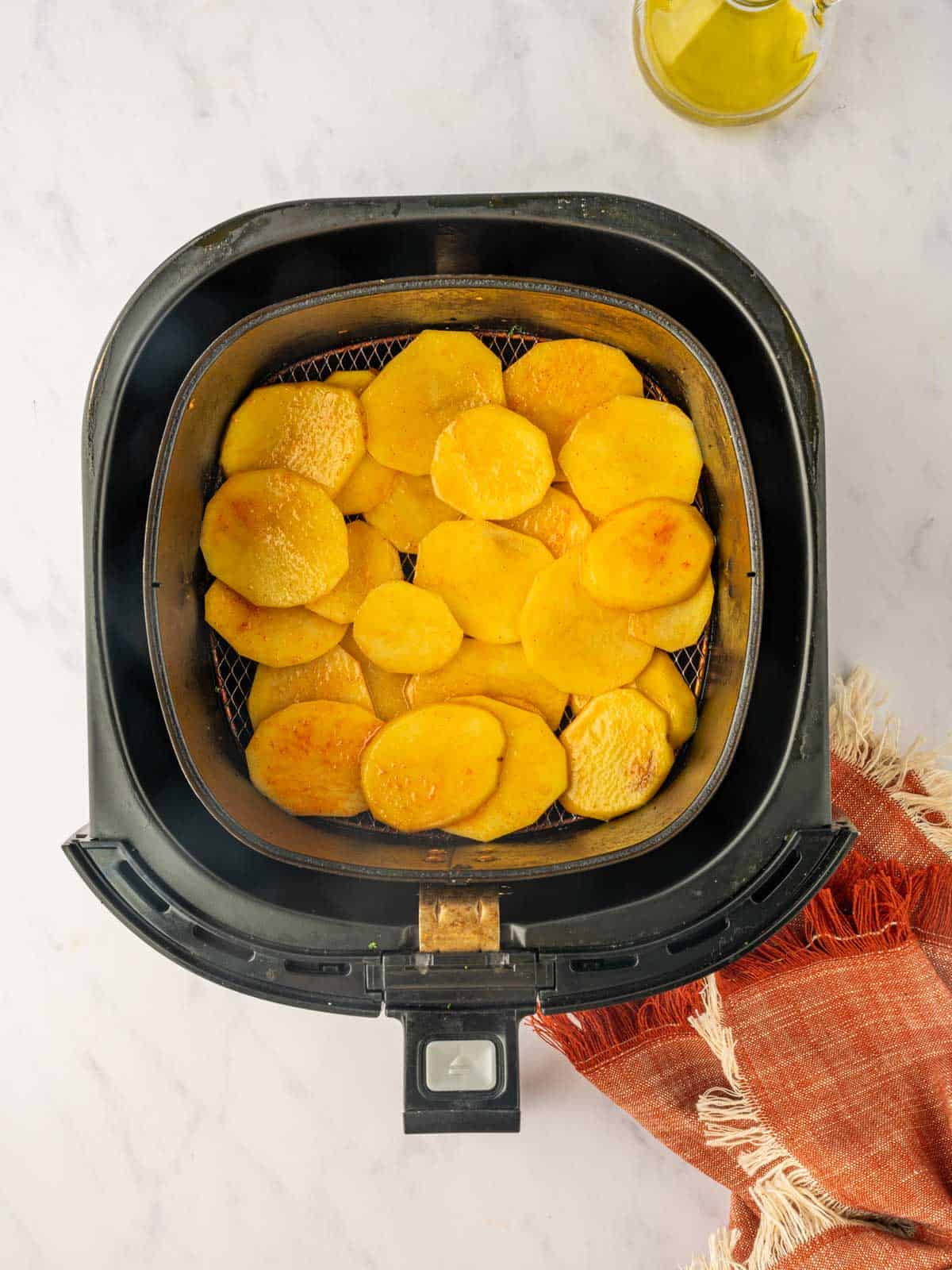 Seasoned potatoes are layered in an air fryer.
