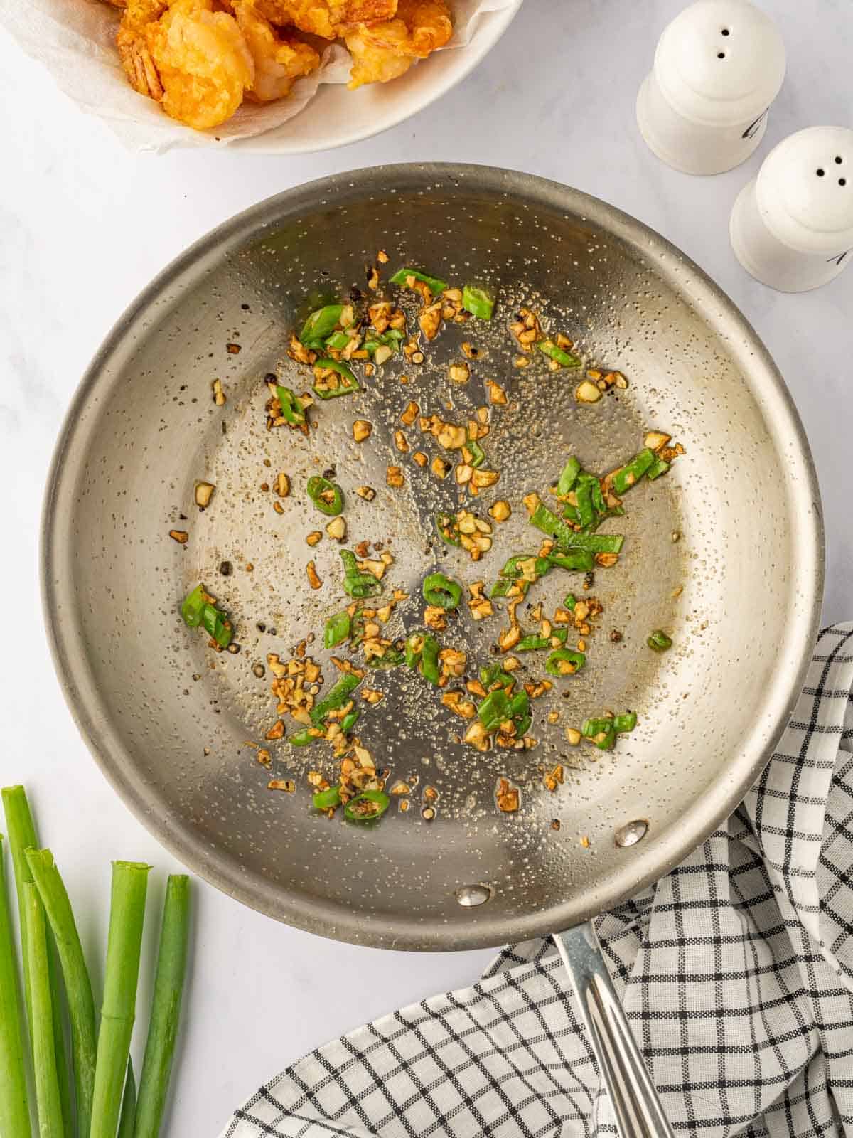 Process of sauteeing garlic and green onion with seasoning to make salt and pepper shrimp.