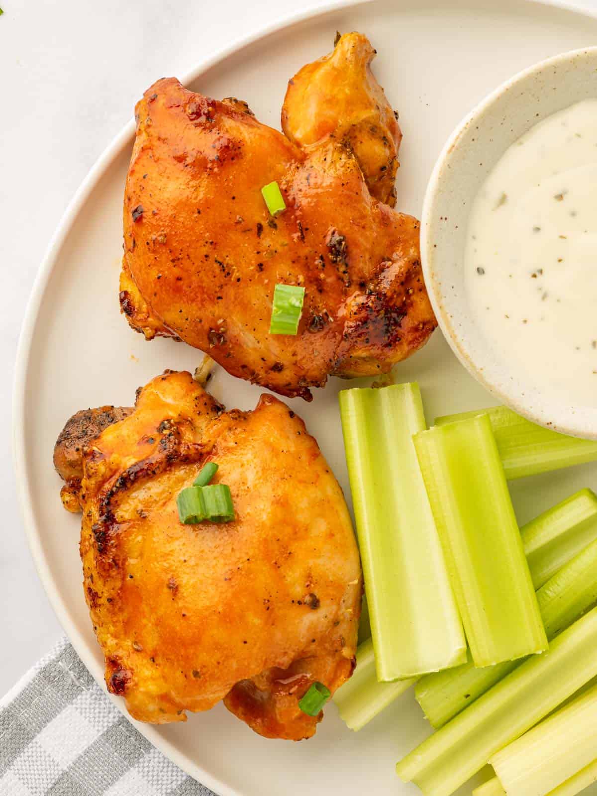 A plate with two spicy chicken thighs, celery sticks and dressing.