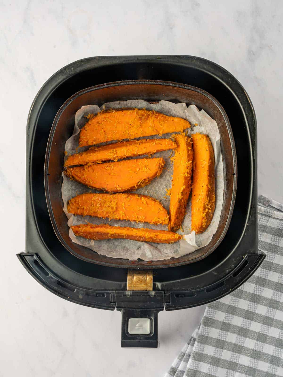 Parmesan coated sweet potatoes in an air fryer basket.