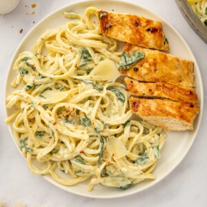 A plate of cheesy pasta served with sliced chicken breast.