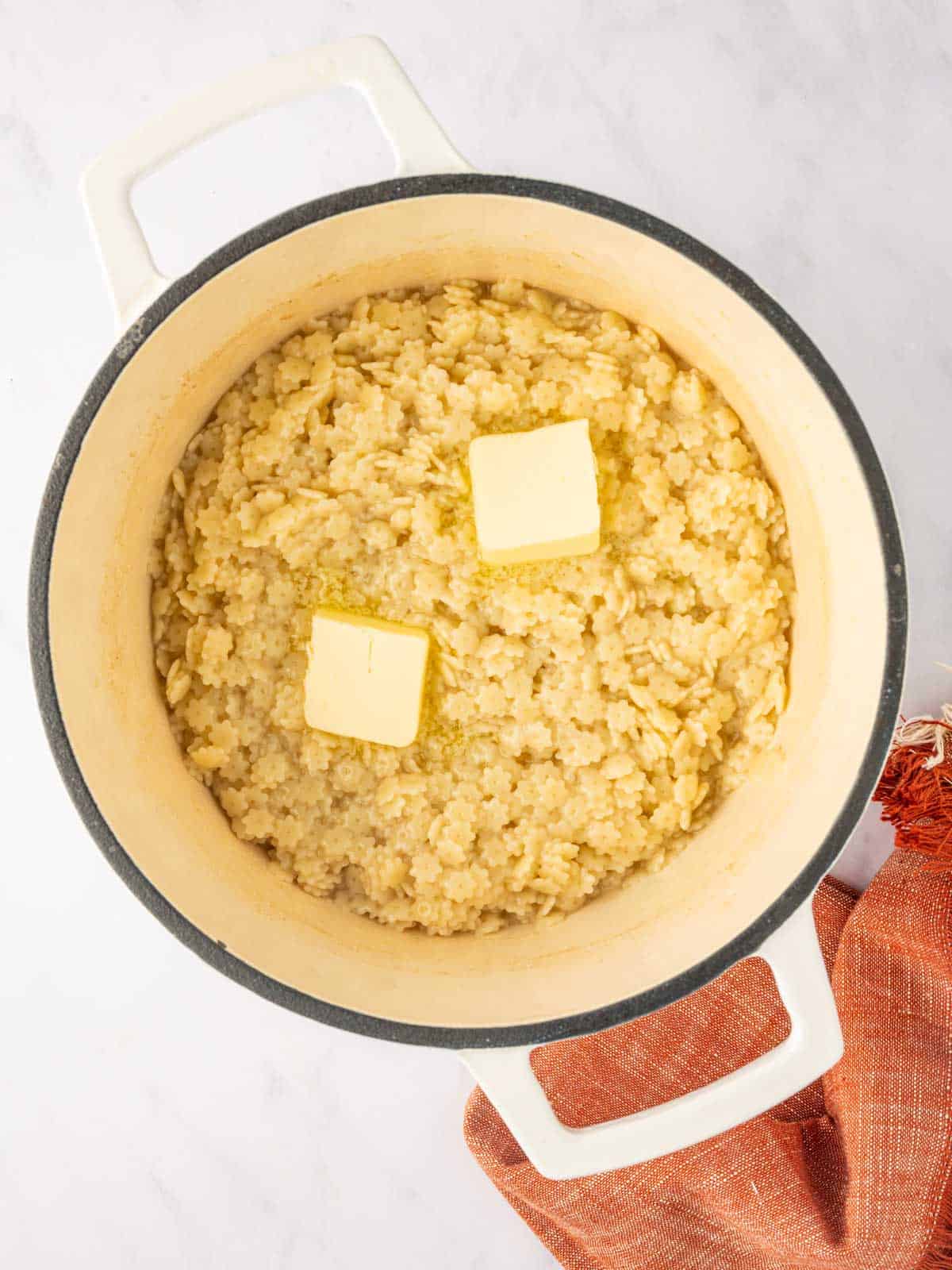 Butter melts over a dutch oven of pasta noodles.