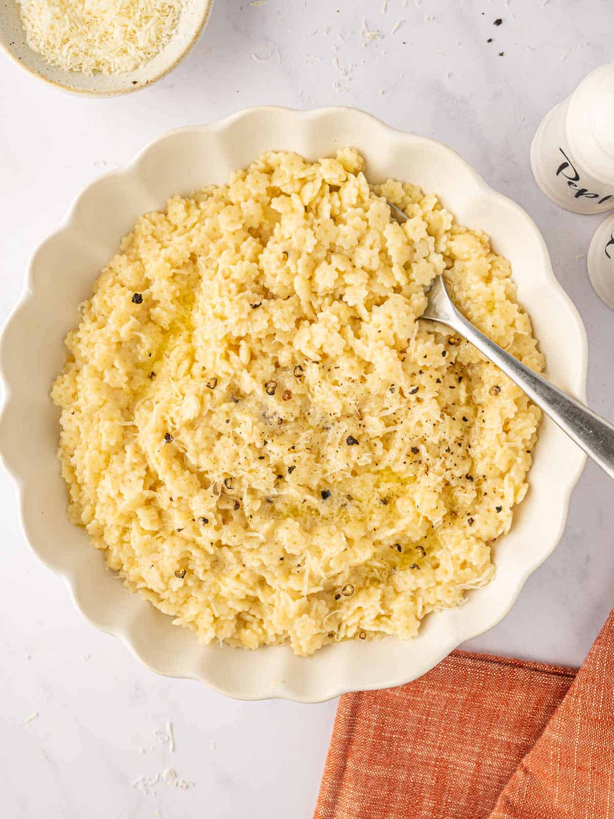 A spoon rests in a white bowl of pastina pasta.