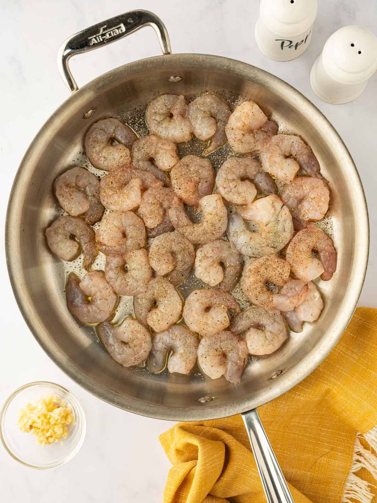 Raw seasoned shrimp in a skillet.