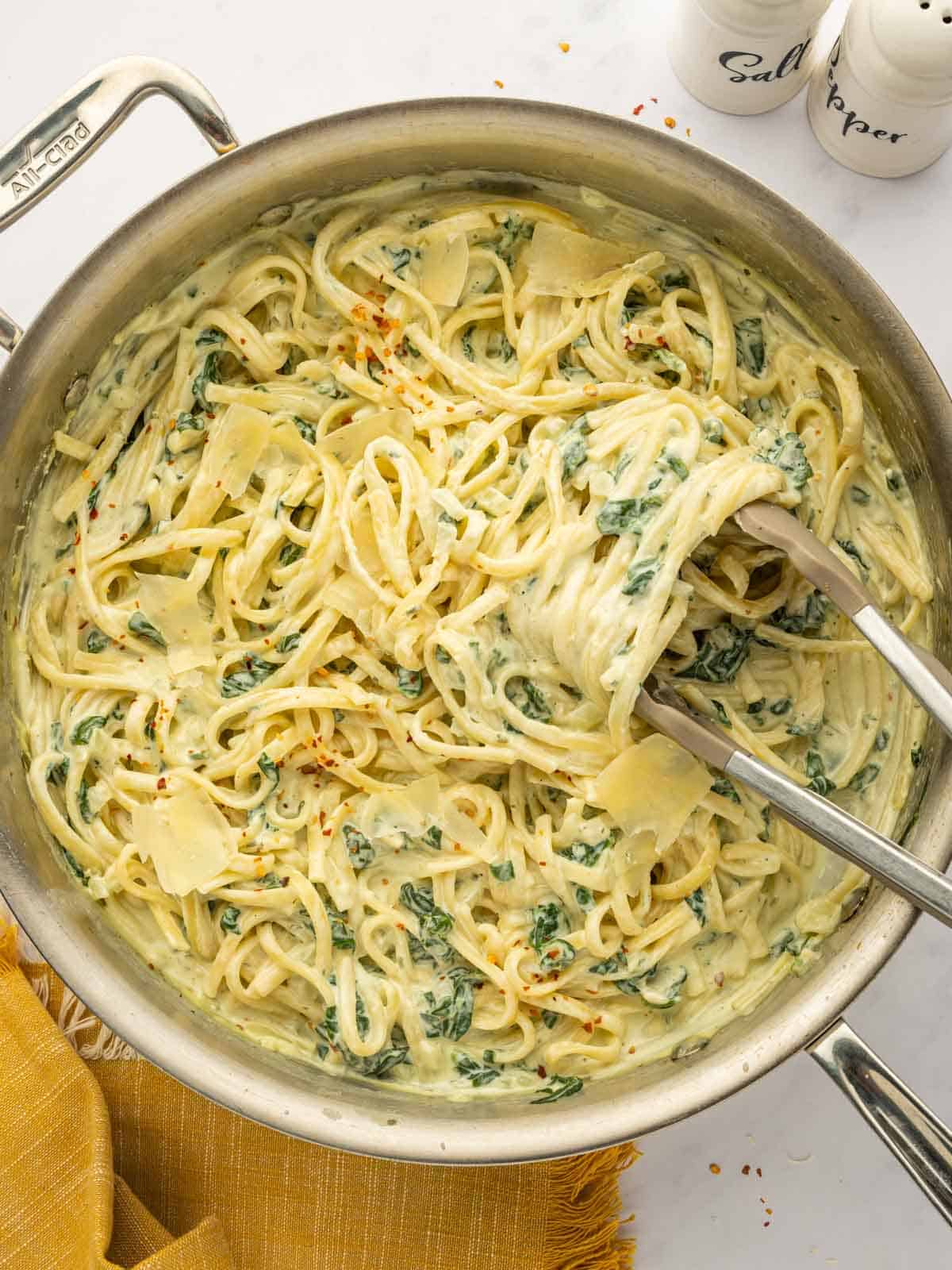 Tongs toss boursin cheese pasta in a skillet.
