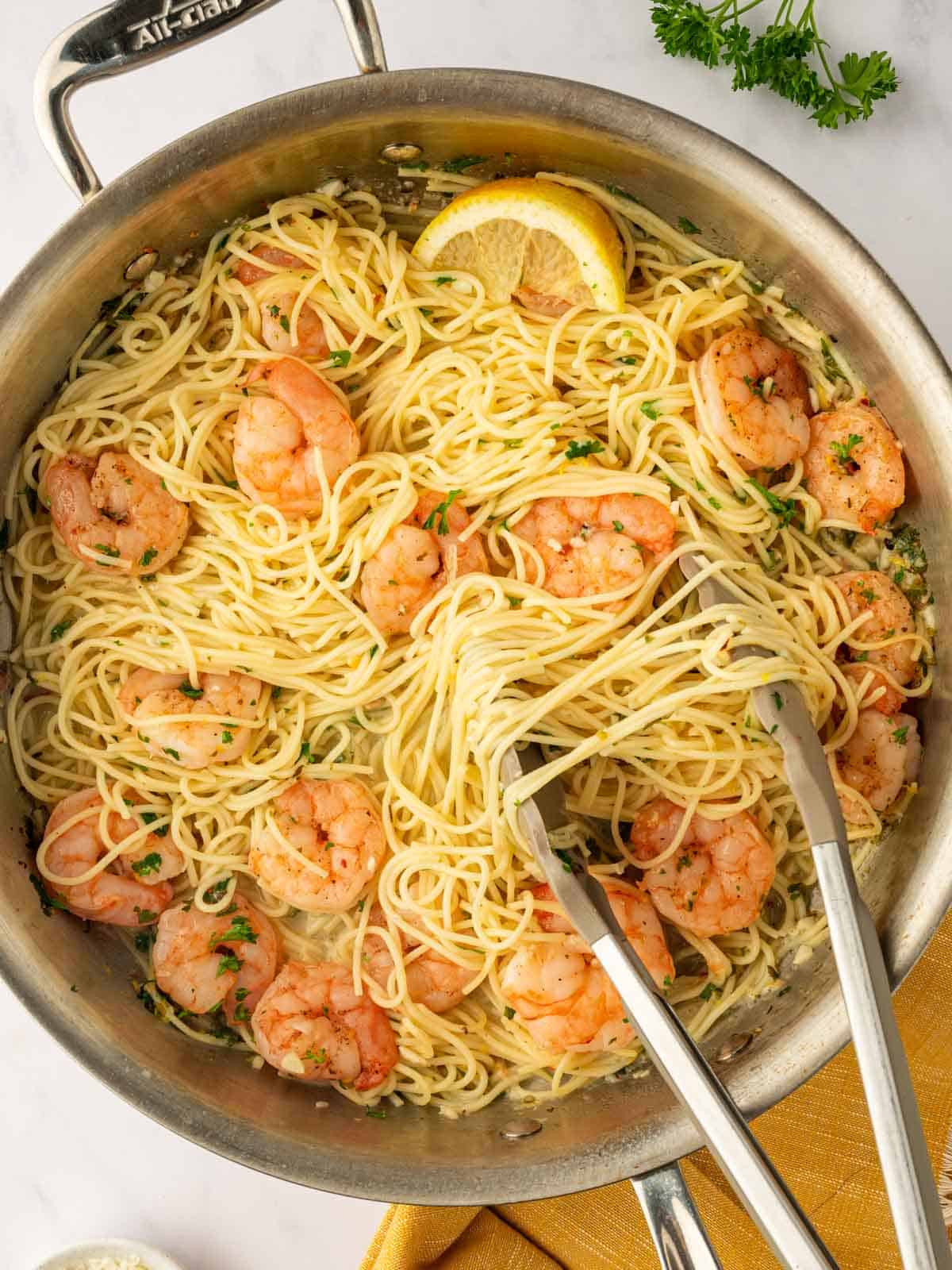 Tongs lift a portion of angel hair pasta from a skillet.