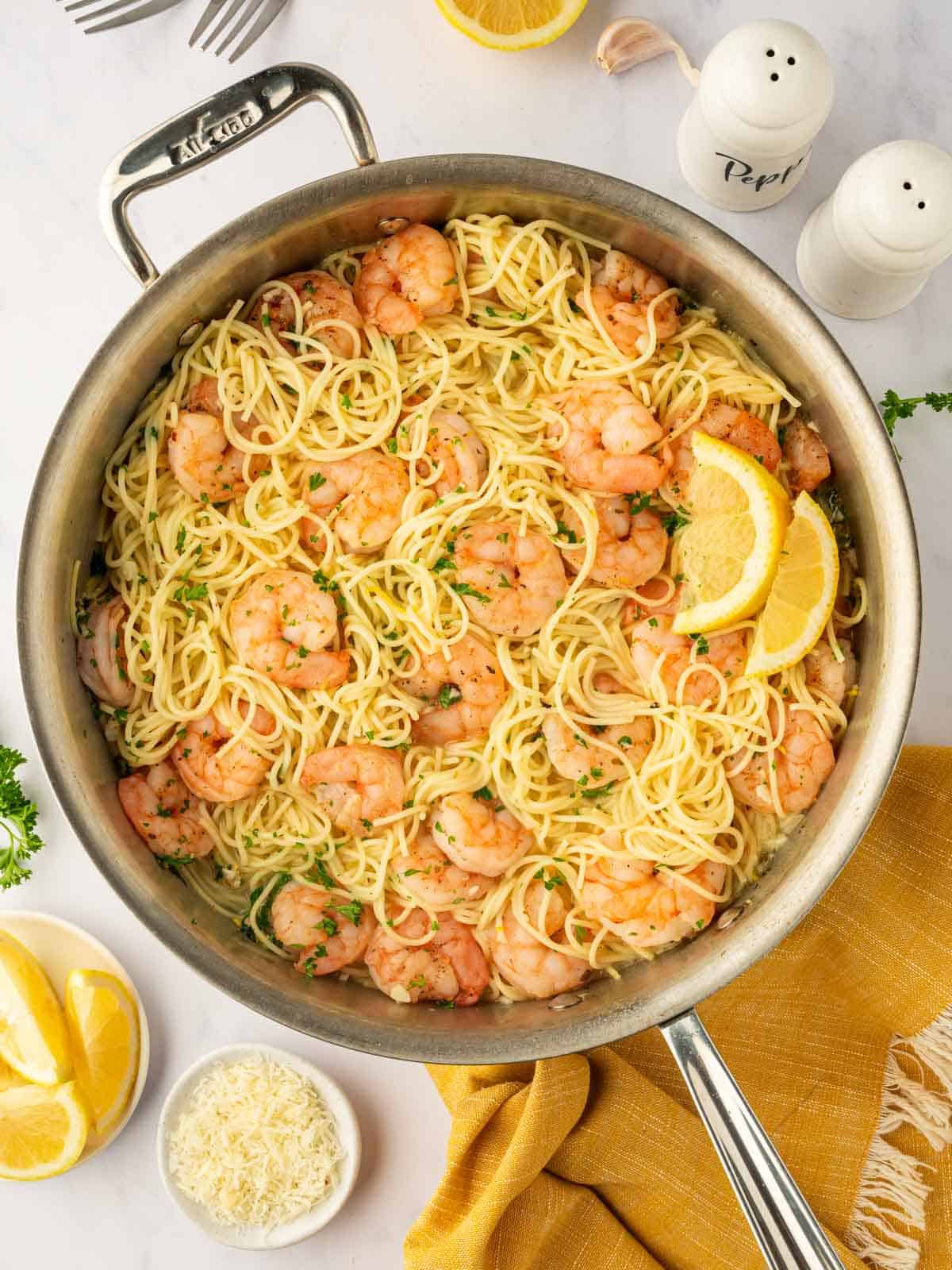 Pasta with shrimp and lemon wedges in a skillet.