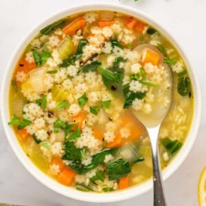 A spoon rests in a bowl of pastina soup.