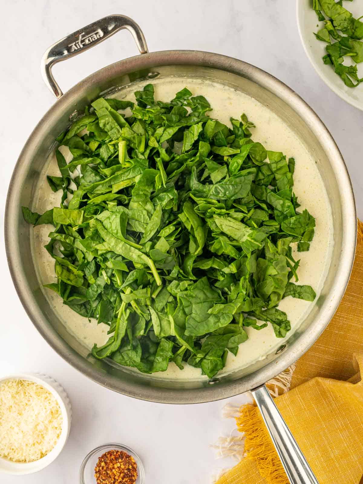 Spinach wilts in a skillet of cream sauce.