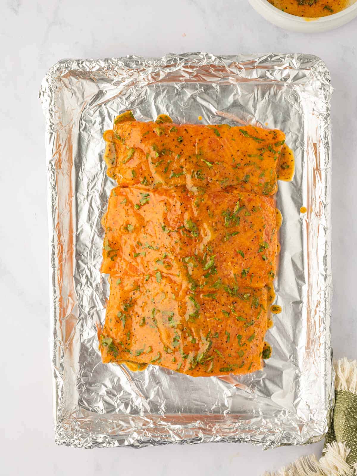 Salmon is topped with the lemon pepper marinade on a foil lined tray.