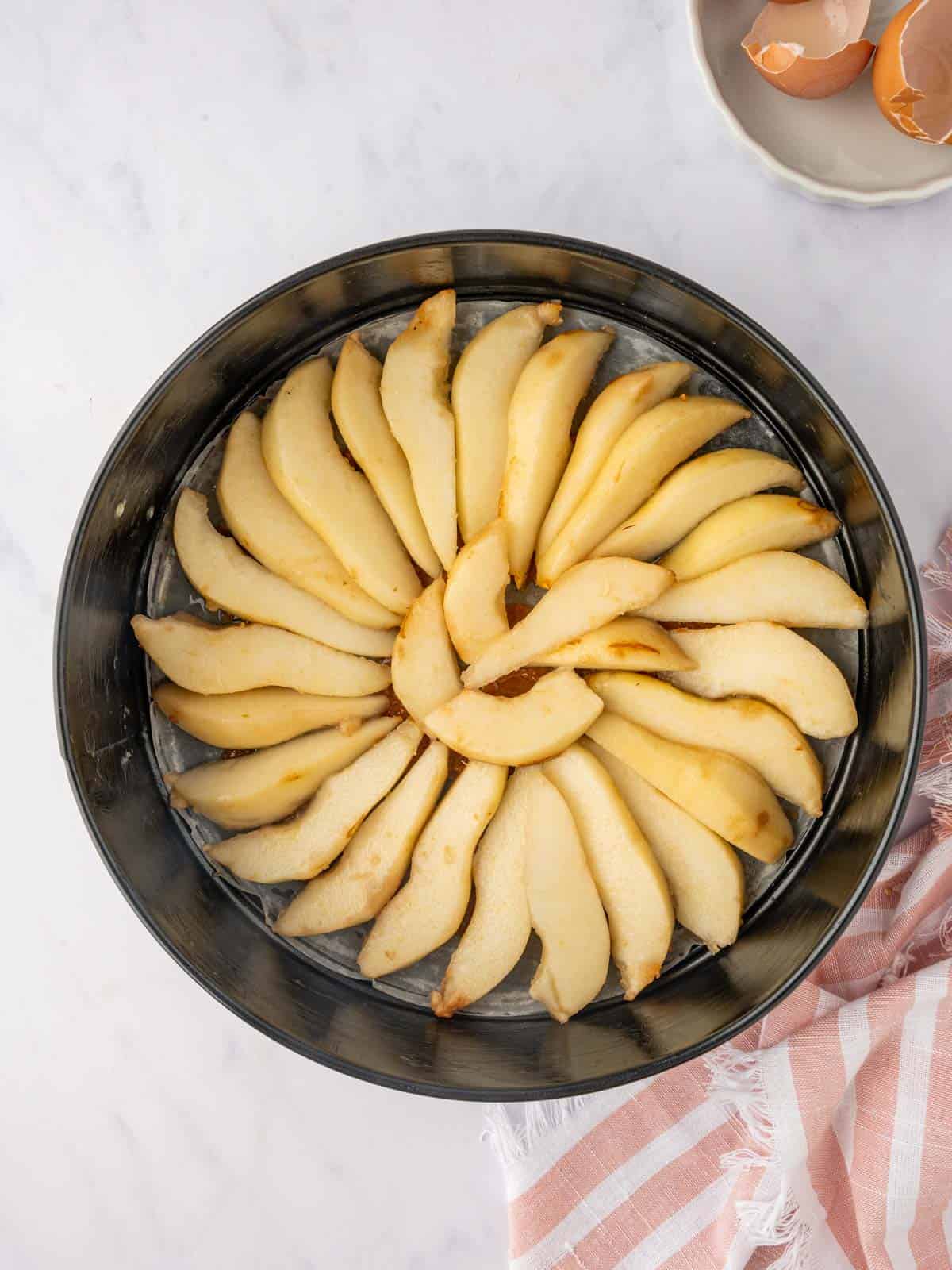 Pear slices are artfully arranged in a cake pan.