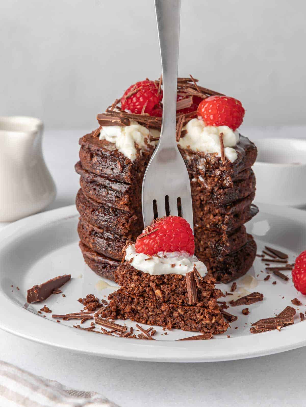 A fork picks up a bite of pancakes topped with raspberries.