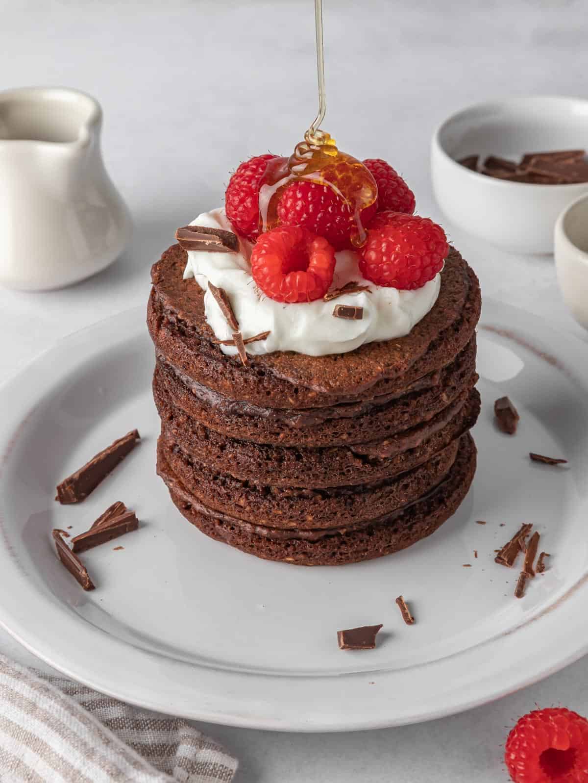 Chocolate protein pancakes topped with wipped cream and raspberries.