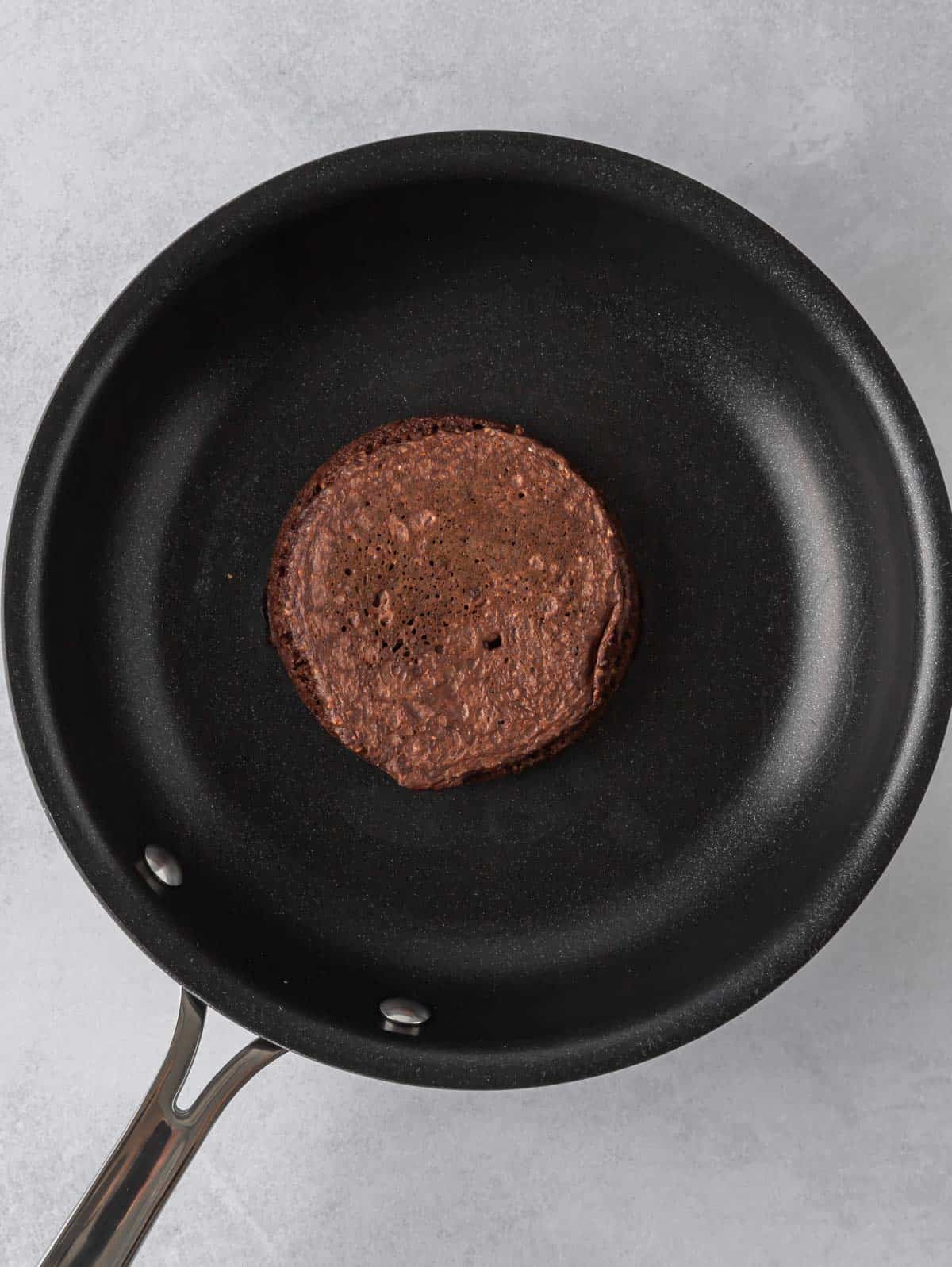 A chocolate pancake cooks in a skillet.