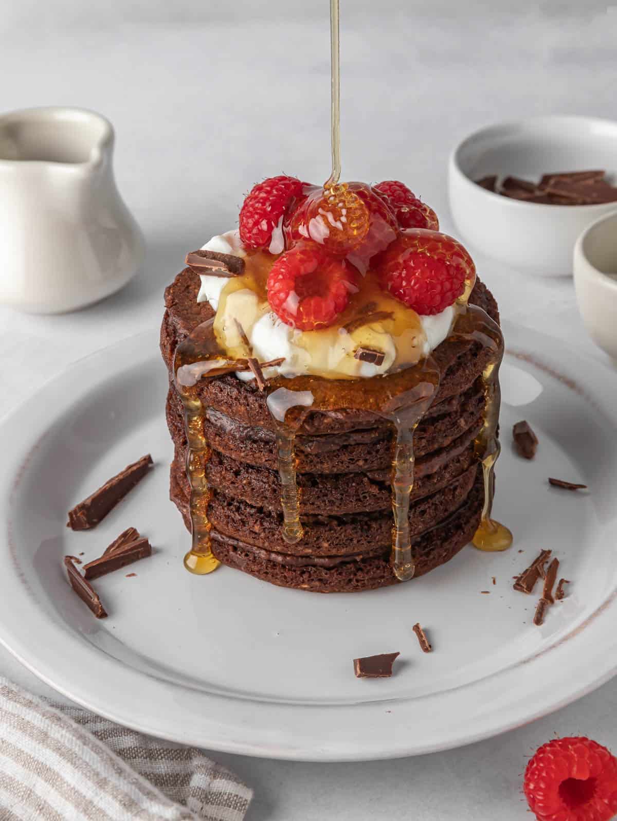 Pancakes on a white plate with syrup being drizzled over them.