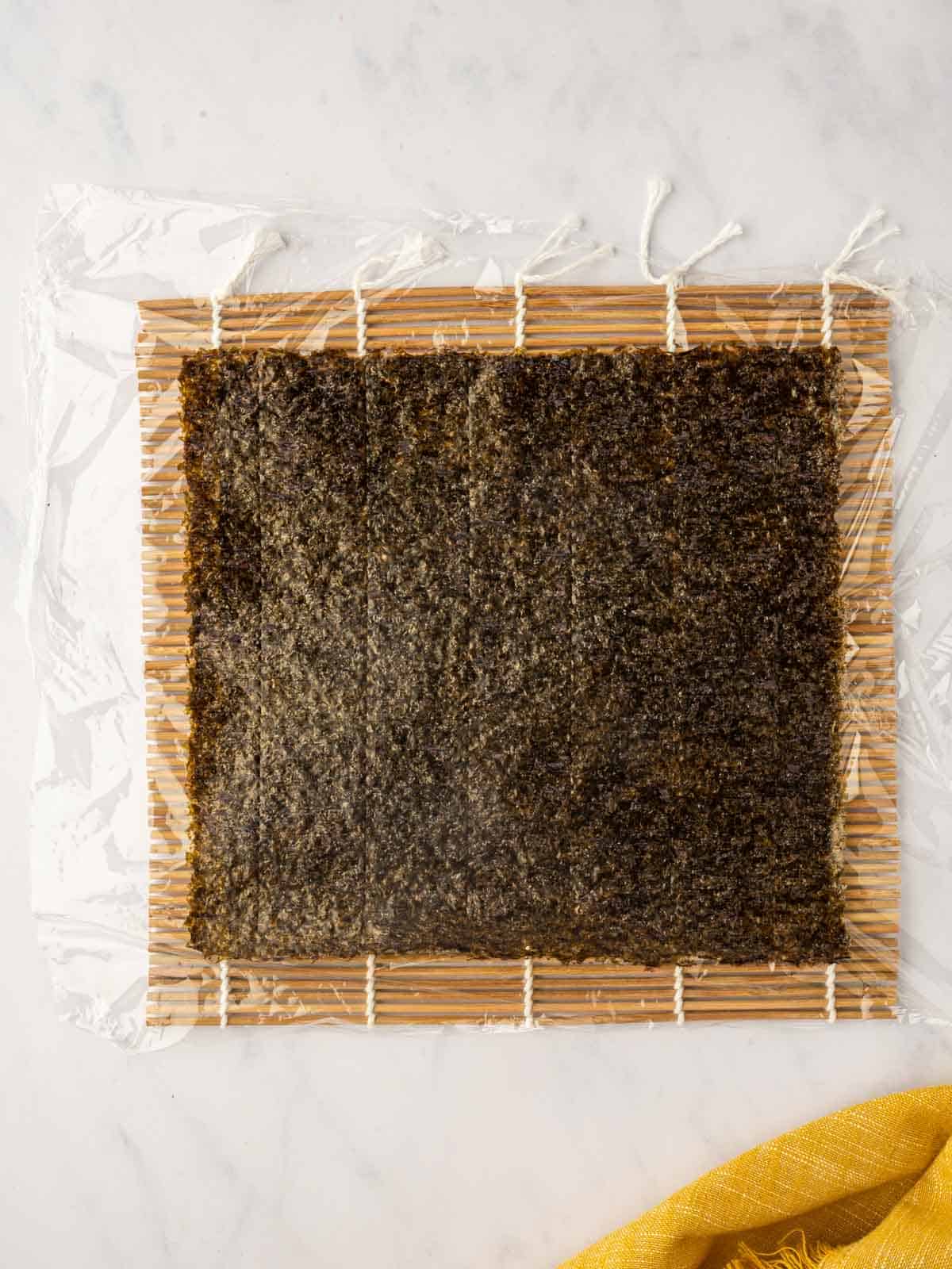 Lay a nori sheet over plastic wrap on a bamboo mat.