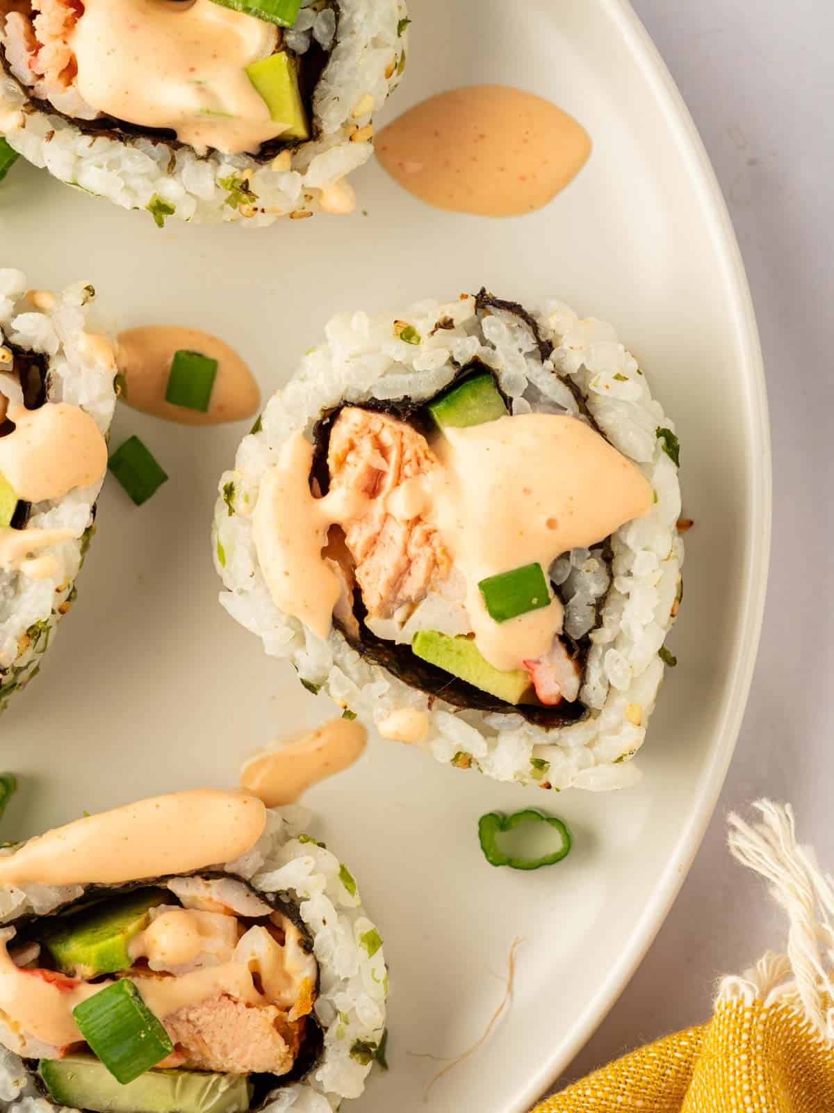 A piece of salmon sushi is topped with spicy mayo.