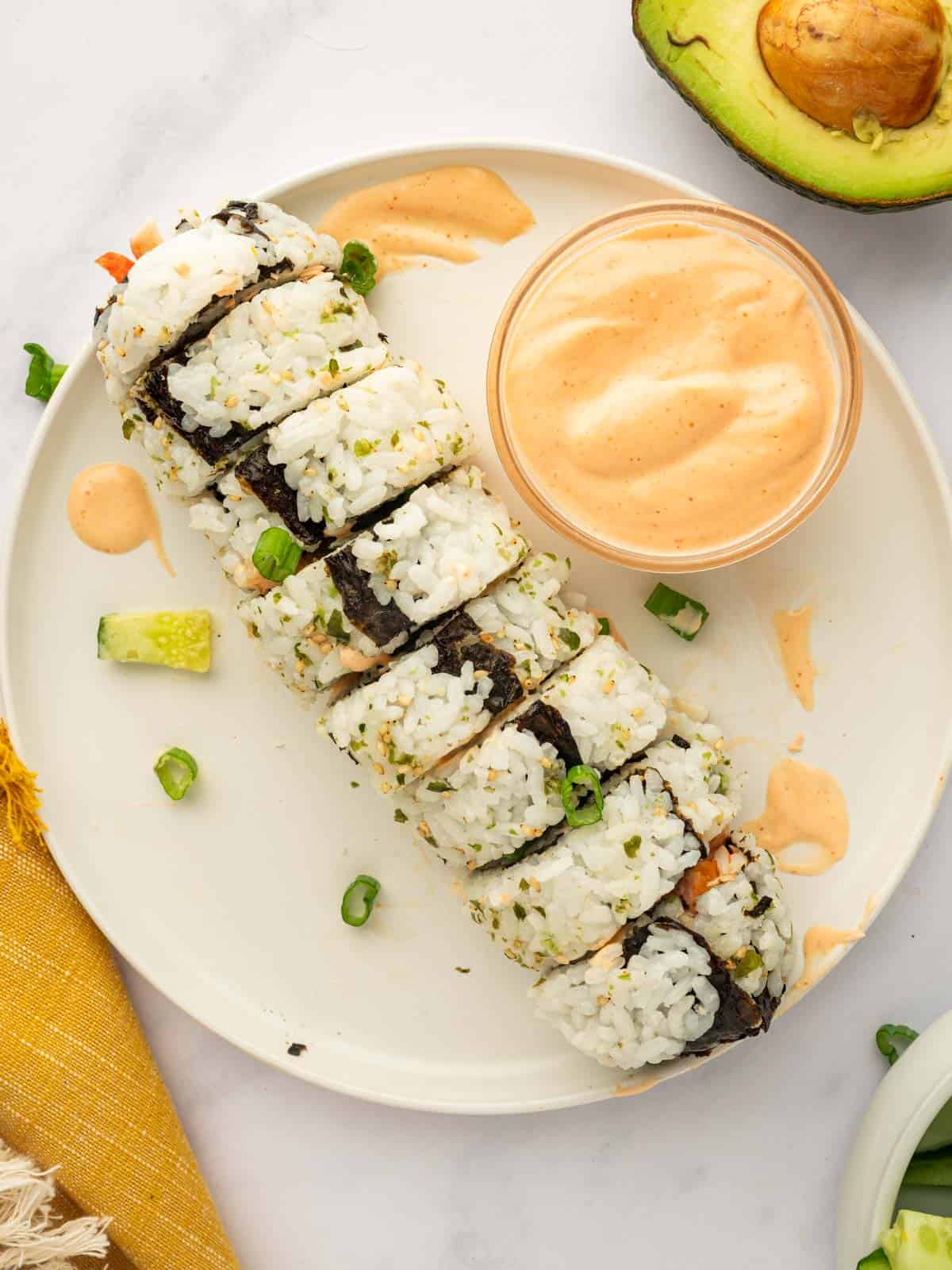 A roll of sliced spicy salmon sushi is on a plate with spicy mayo.