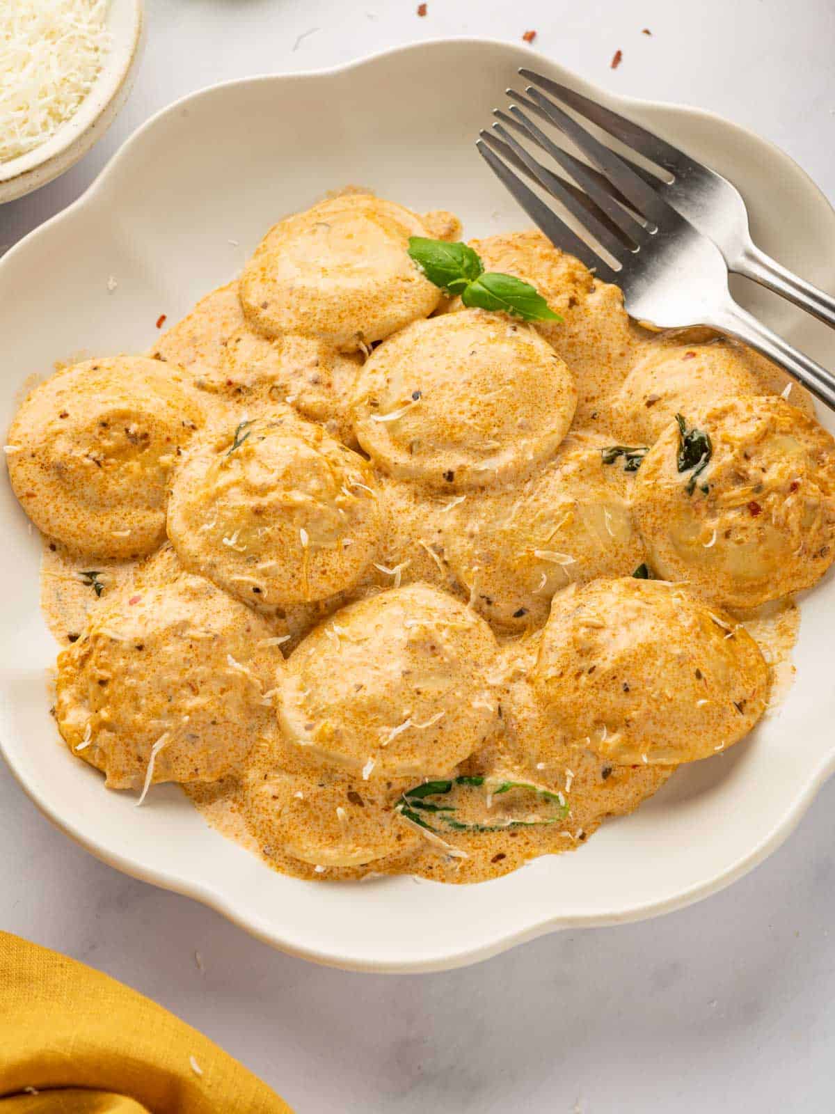 A fork rests beside a plate of ravioli topped with a creamy red sauce.