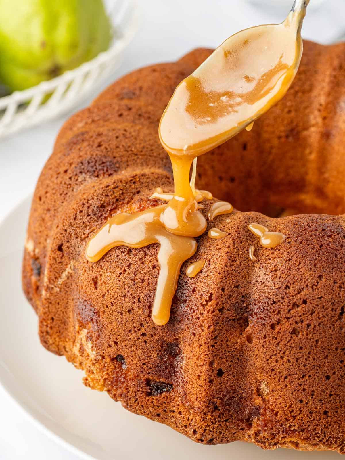A spoon drizzles caramel on a cooled bundt cake.