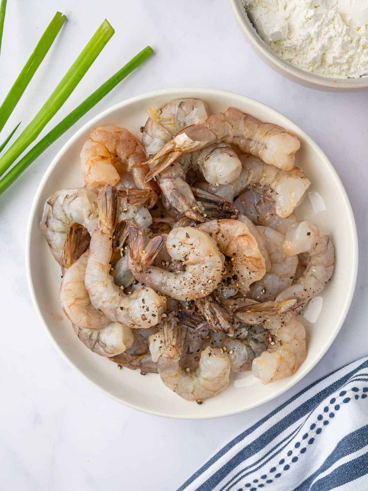 Raw shrimp is seasoned with salt and pepper in a bowl.