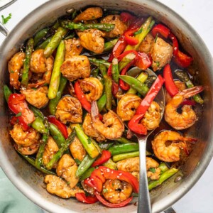 A spoon serves stir fry with chicken and shrimp.