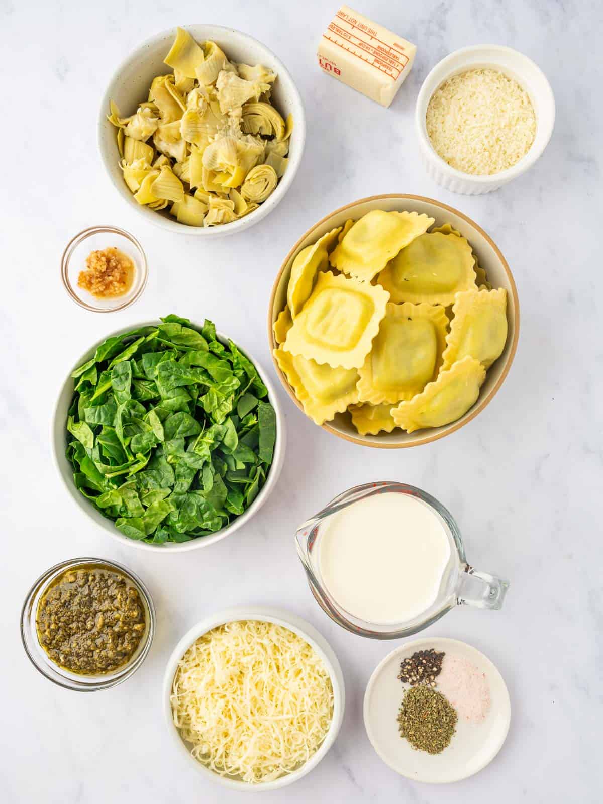 Ingredients for spinach artichoke ravioli bake laid out, including cheese ravioli, spinach, artichoke hearts, and cream cheese.