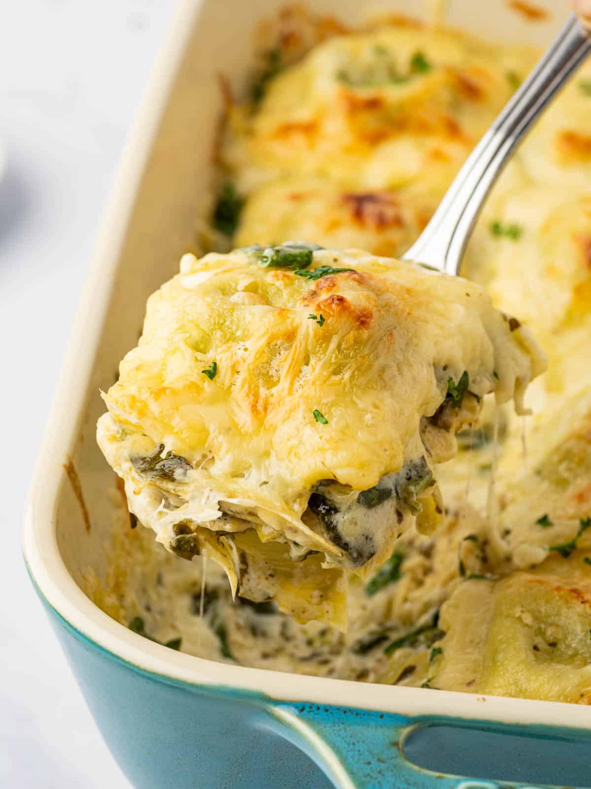Close-up of cheesy spinach artichoke ravioli bake lifted from the dish.