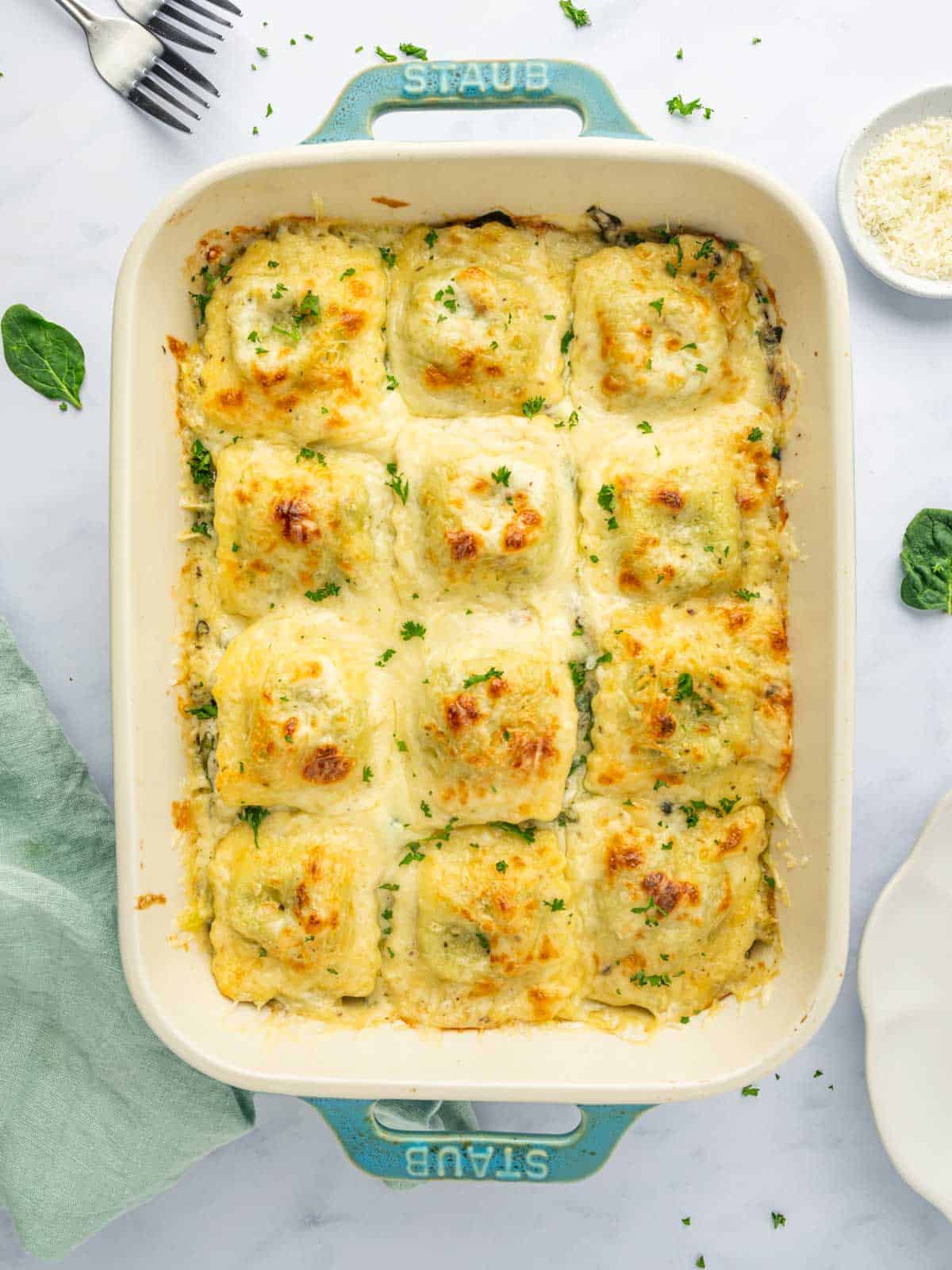 Overhead shot of spinach artichoke ravioli bake in a white baking dish, golden melted cheese on top.