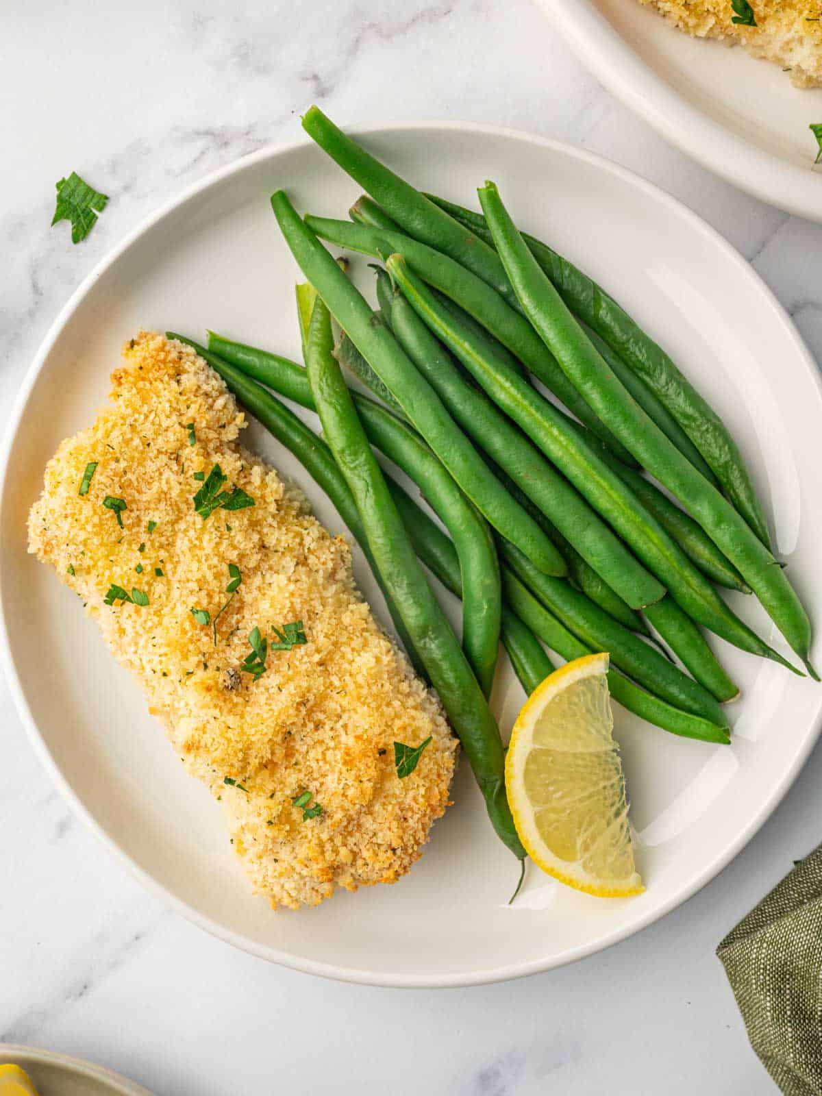 Baked cod on a plate with green beans.