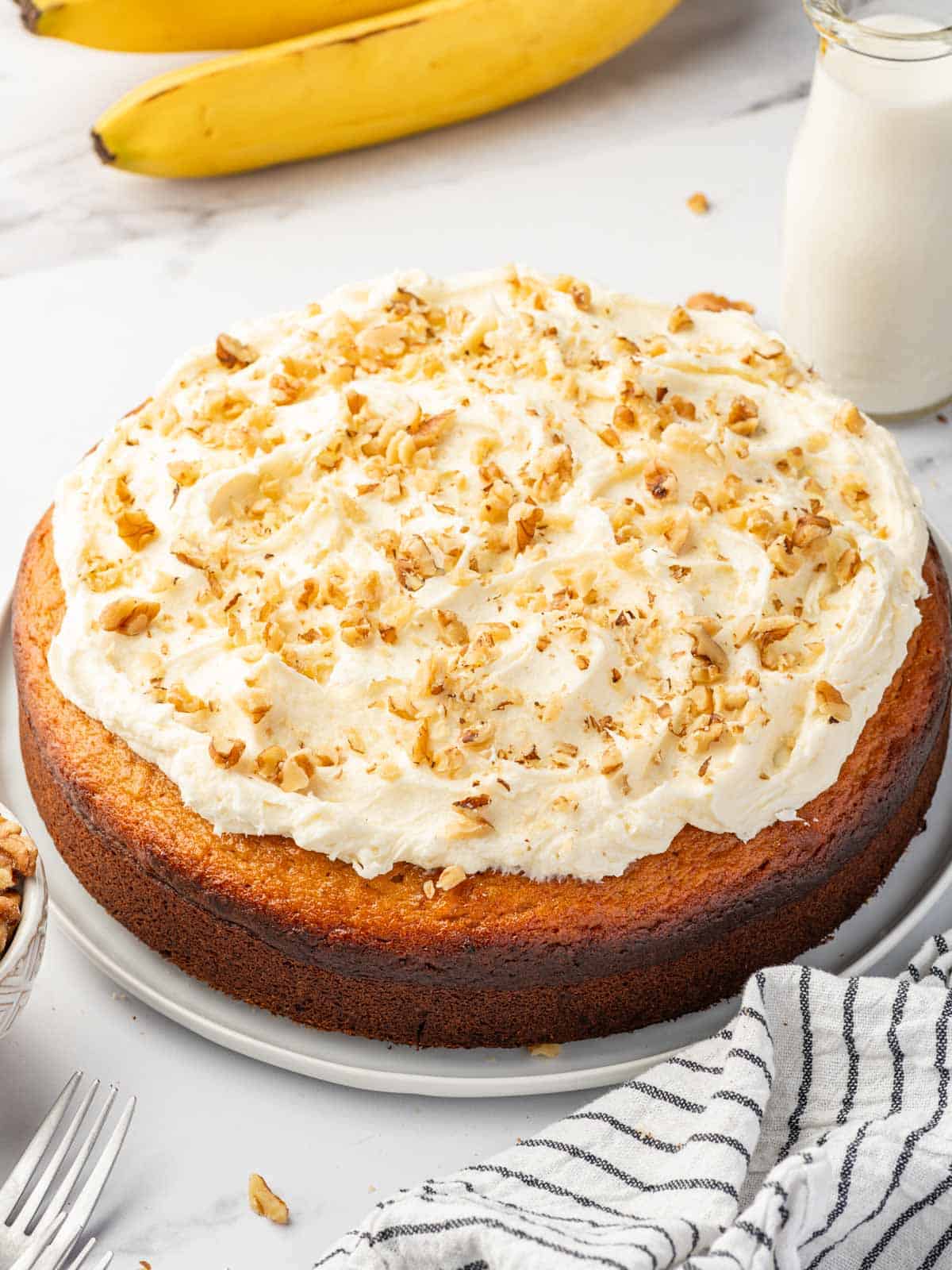 Banana walnut cake with a layer of cream cheese frosting topped with walnuts on a platter.