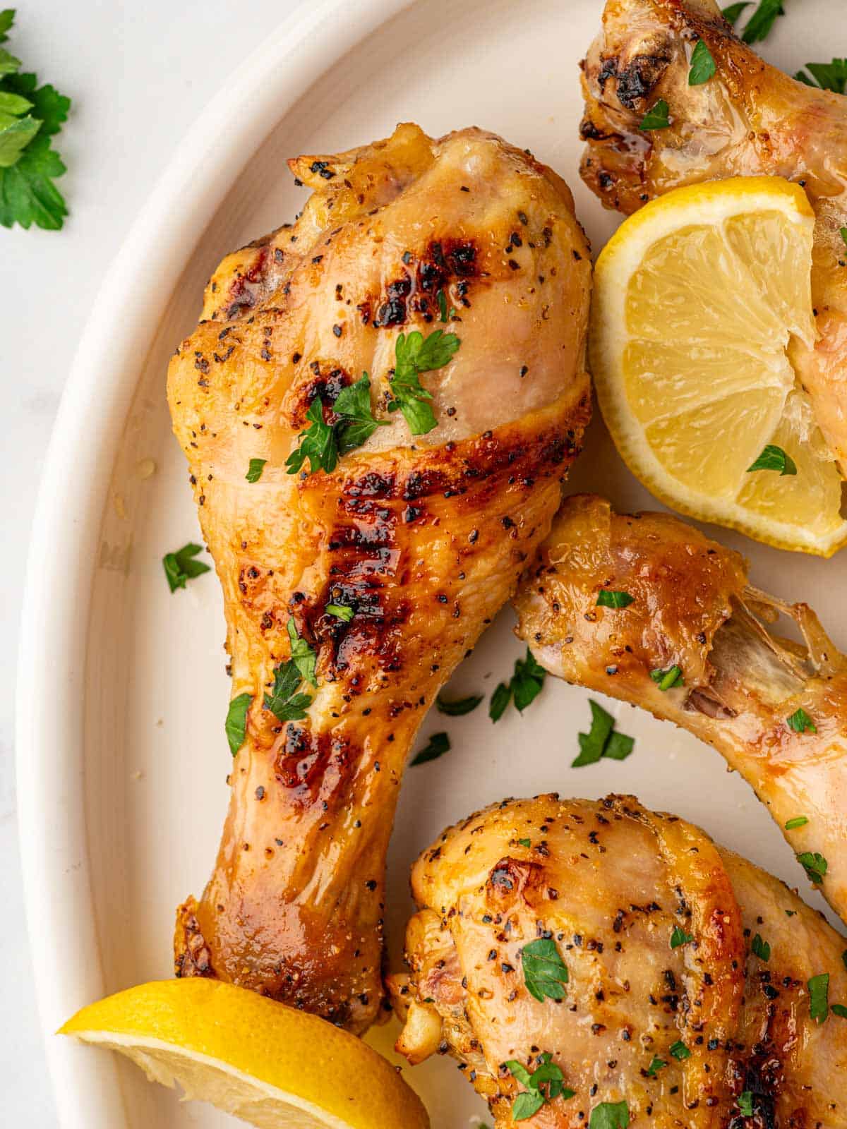 Closeup of a baked chicken leg with lemon pepper seasoning on a plate with lemon wedges.