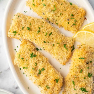 Baked cod filets on a plate garnished with parsley and lemon slices.