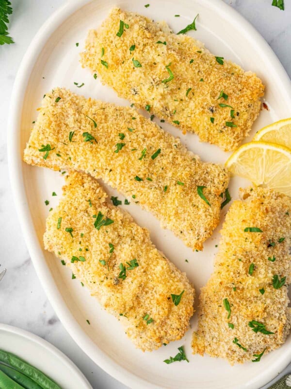 Baked cod filets on a plate garnished with parsley and lemon slices.