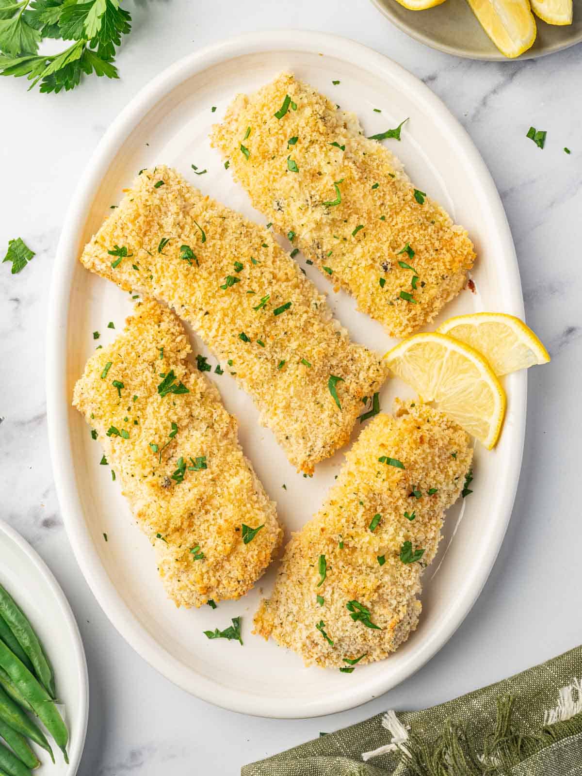Crispy golden panko crusted cod fillet served on a plate with lemon wedges.