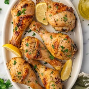 A platter with baked lemon pepper chicken drumsticks with lemon wedges.