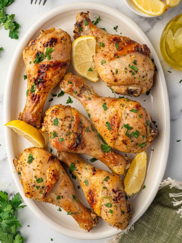 A platter with baked lemon pepper chicken drumsticks with lemon wedges.