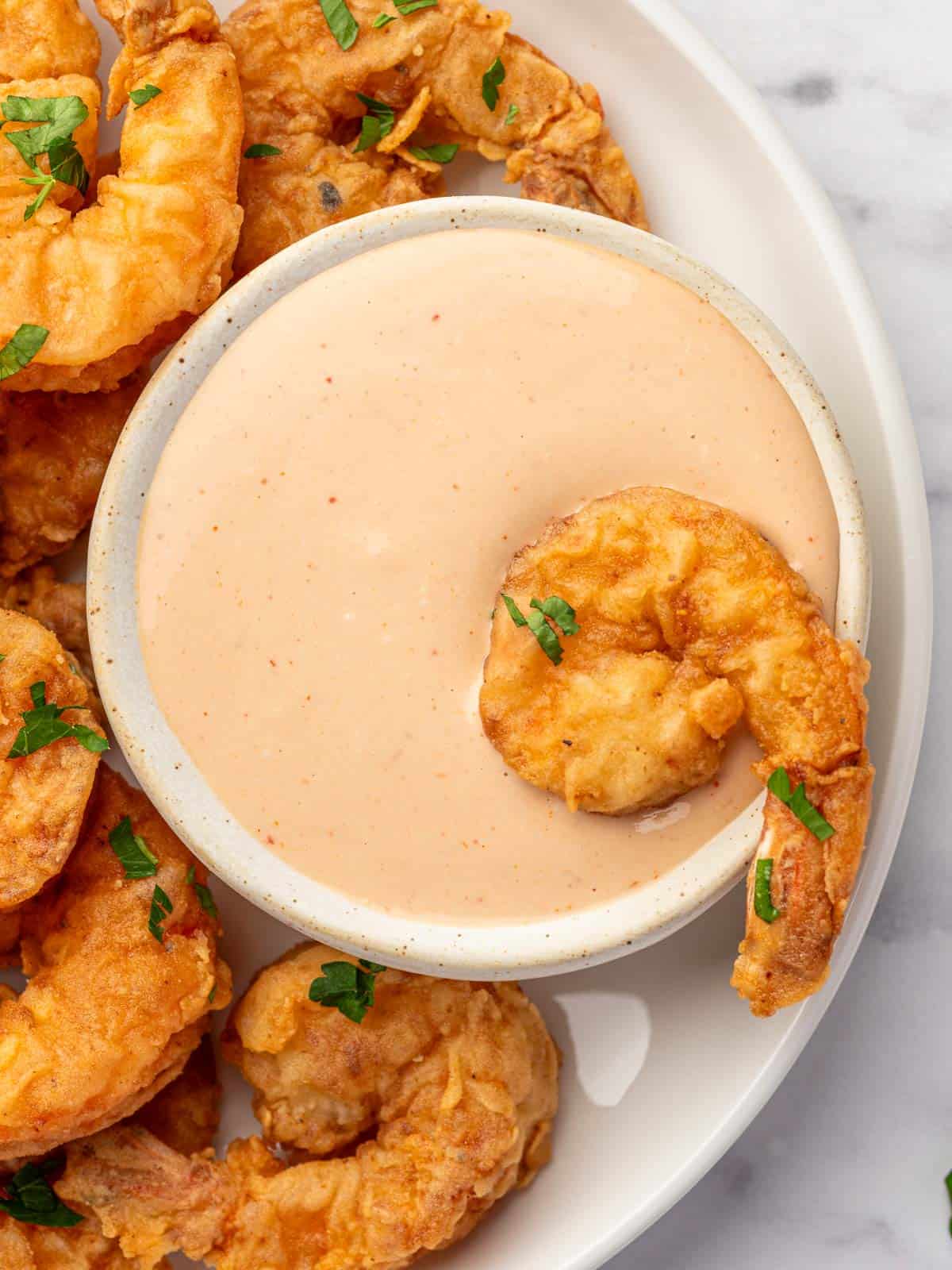A piece of fried shrimp is dipped into a flavorful sauce.