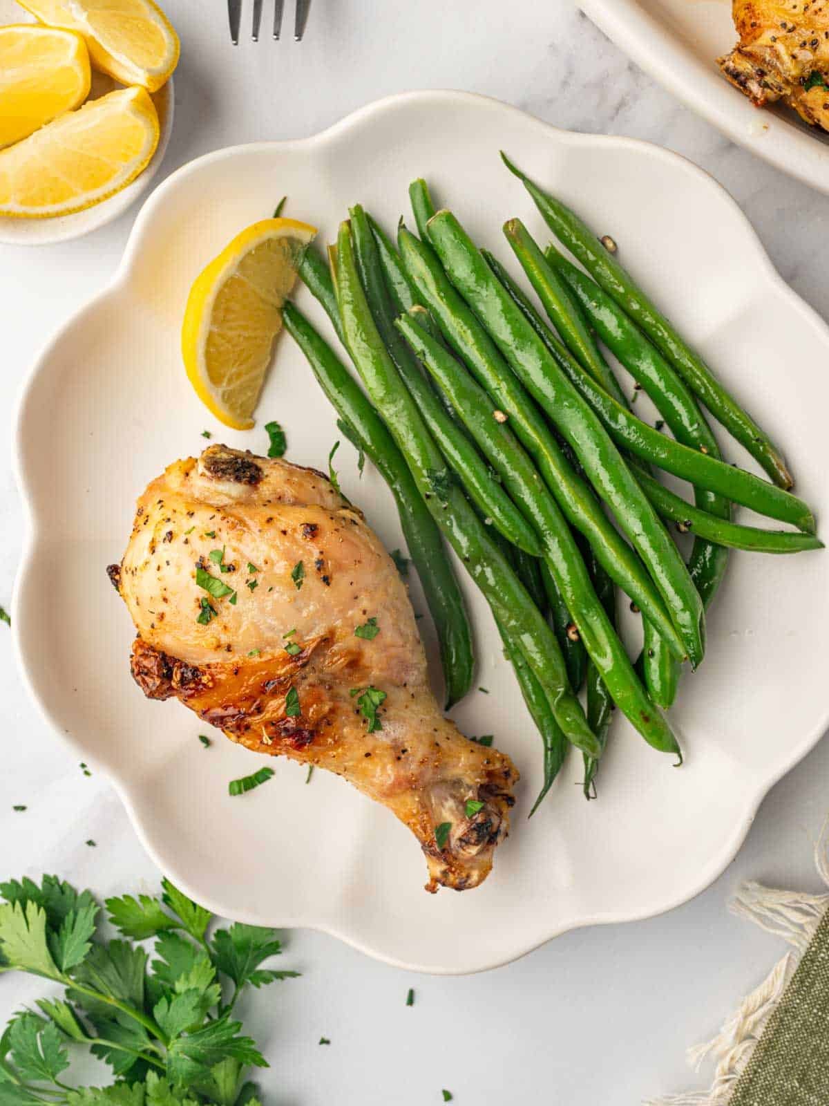 Baked lemon pepper chicken drumstick on a plate with green beans.