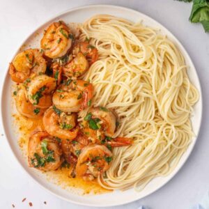 Garlic shrimp with cilantro and orange-red sauce served alongside angel hair pasta.