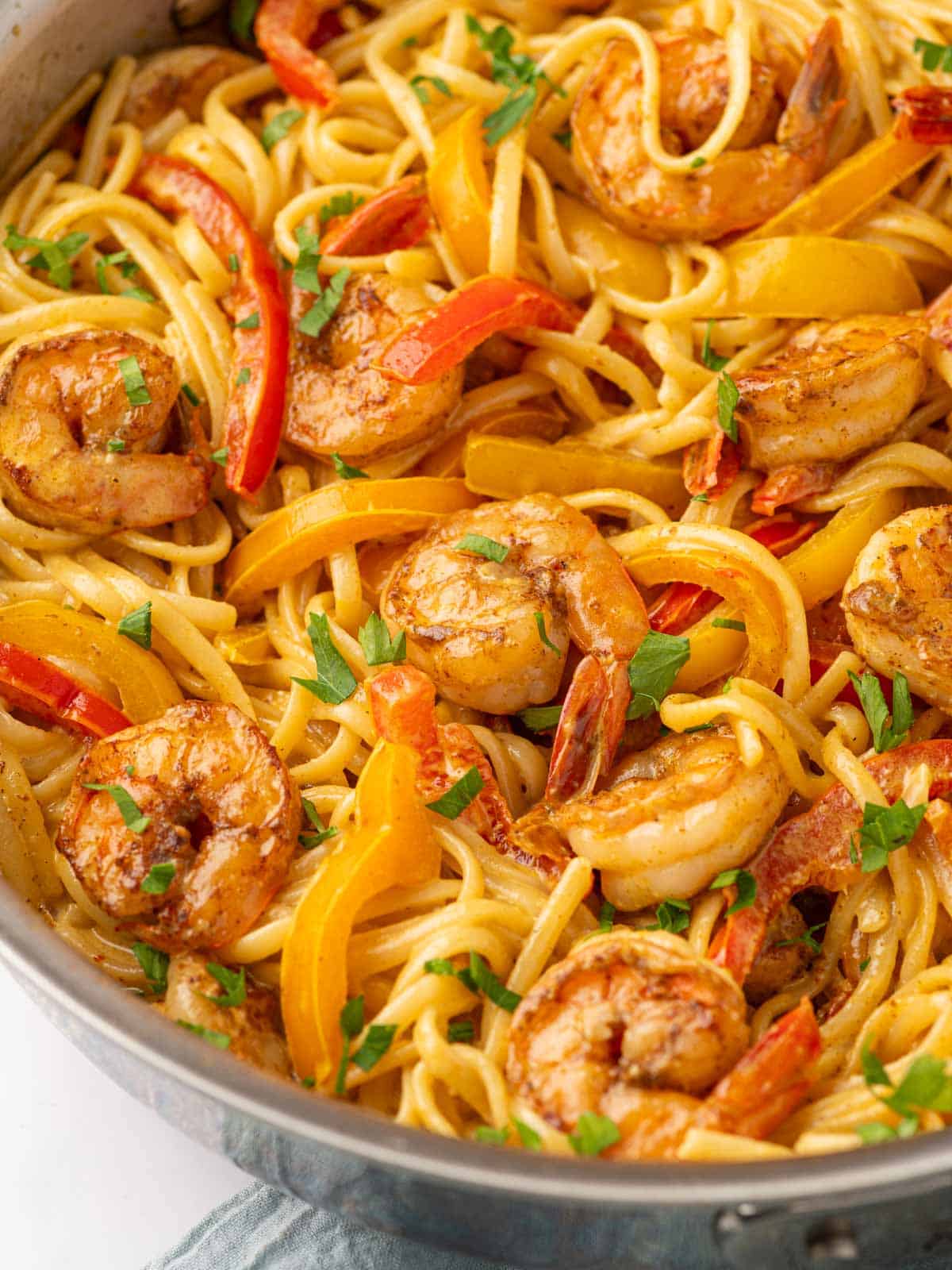 Close up picture of spicy shrimp mixed with bell peppers and pasta and garnished with parsley.