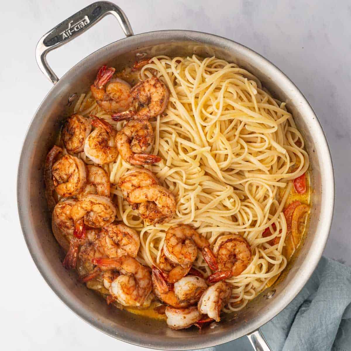 Cooked shrimp is tossed with cooked pasta in a skillet.