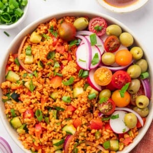 Bowl of turkish kisir salad garnished with tomatoes, olives and radish.