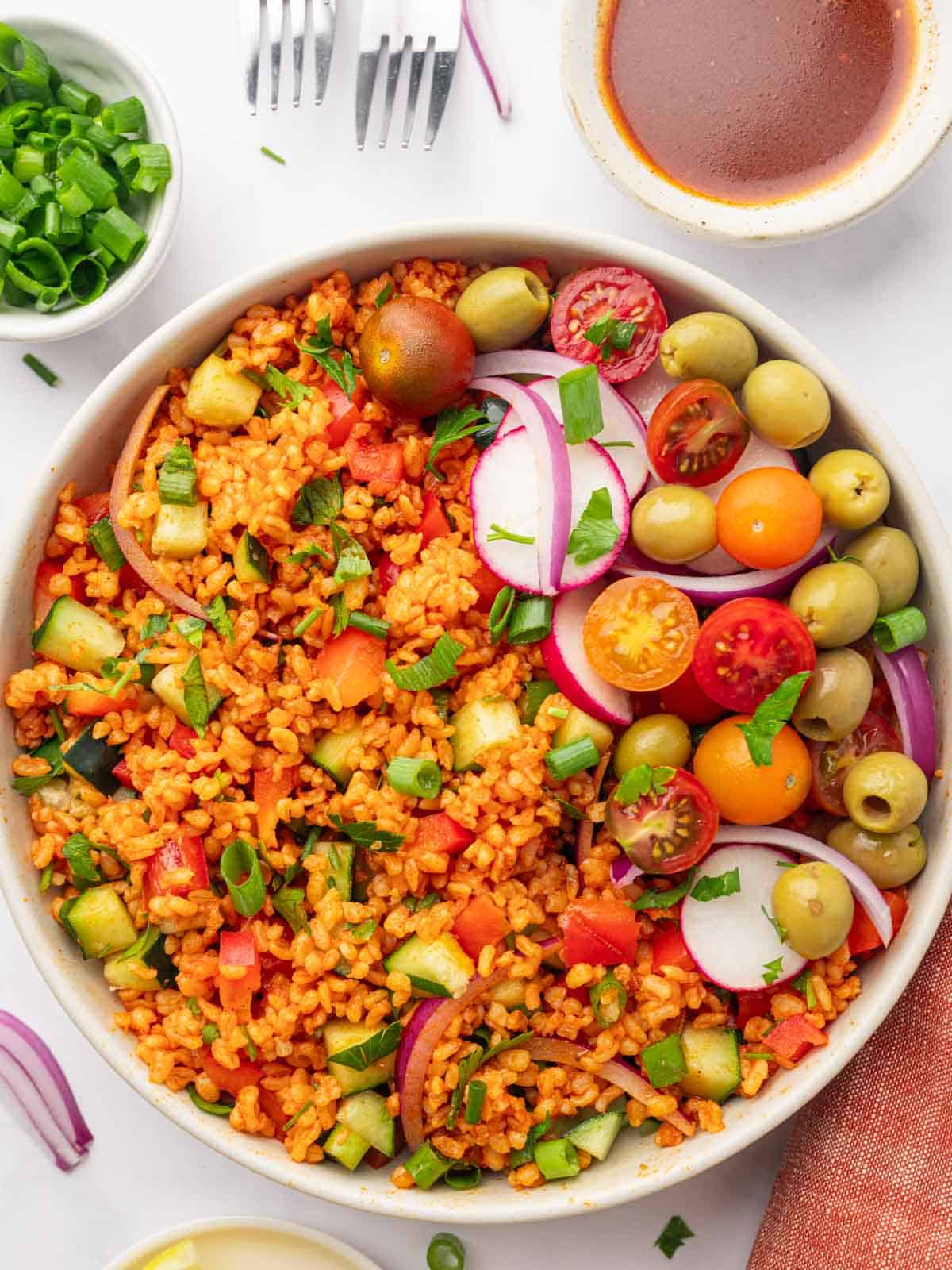 Bowl of turkish kisir salad garnished with tomatoes, olives and radish.