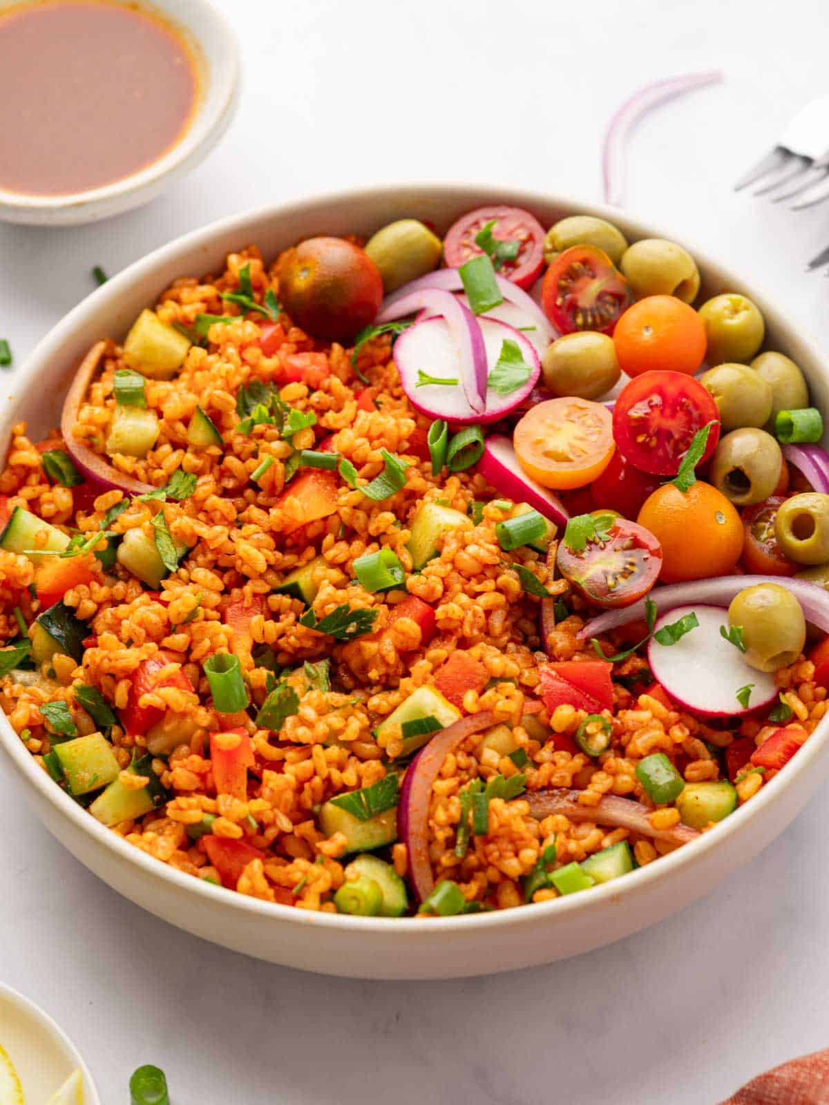 Bowl of turkish kisir salad garnished with tomatoes, olives and radish.