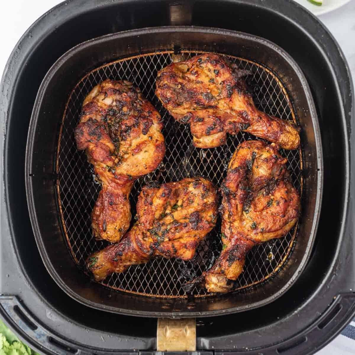 Butterfly drumsticks cooking in an air fryer basket.